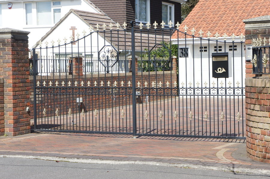 Black metal driveway gates with gold finials between brick piers