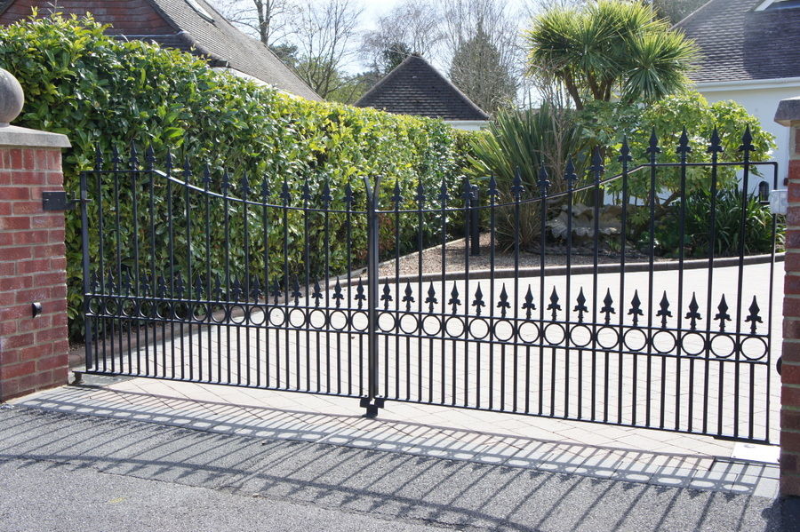 Black metal driveway gates with a curved top, spear finials and a band of rings