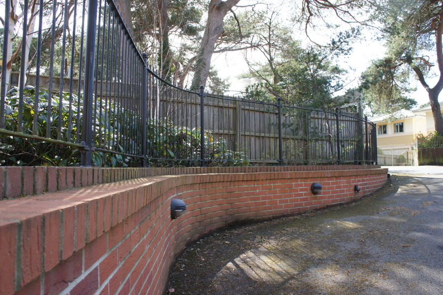 Black railings stepping along a curved brick retaining wall with wall lights