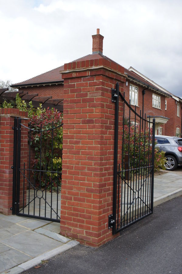 Tall black metal garden gates with a curved top hung from a red brick pier