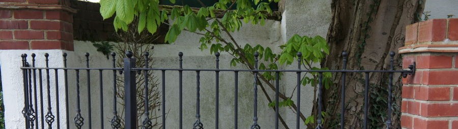 Black railings with twisted basket details between brick piers in front of a tree