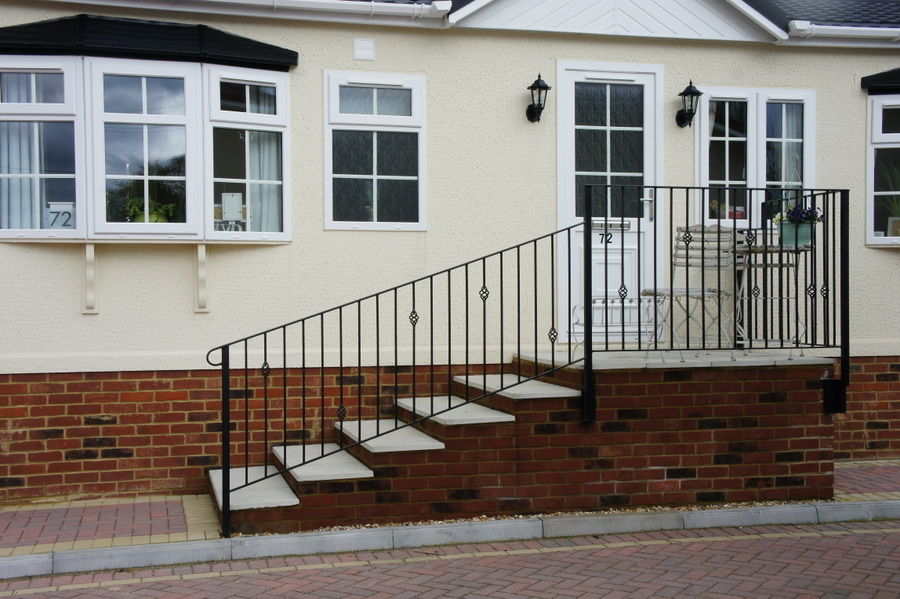 Black metal handrail running up brick steps to a park home front door