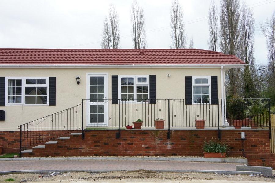 Long raised terrace with black railings and steps across the front of a park home