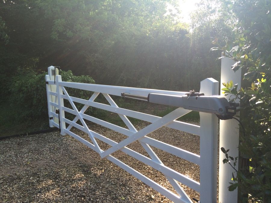 White five-bar gate with a diagonal brace and a gate opener on a gravel entrance
