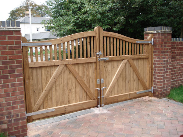 Timber double gates with an arched spindle top and diagonal braces between brick piers