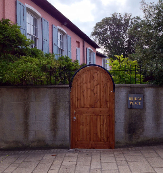 Arched timber pedestrian gate set into a rendered garden wall