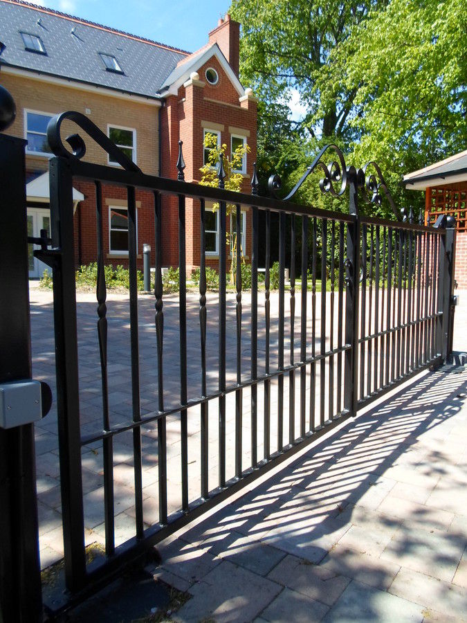 Long black metal sliding gate on a ground track with a scroll detail at the end