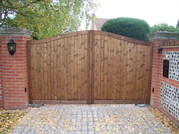 Pair of close-boarded timber gates with a curved top between brick and flint piers
