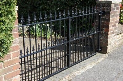 Black metal gate with fleur-de-lis spear tops between brick piers