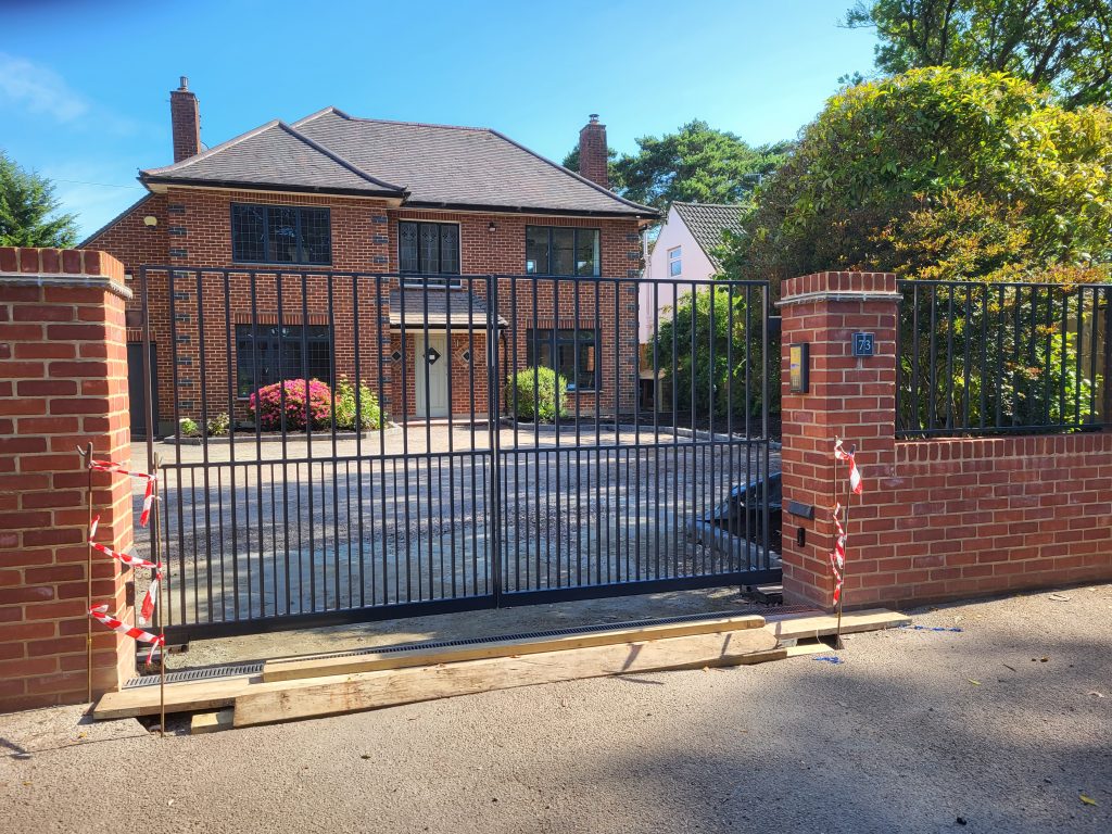 Large black flat-top metal gate being installed between brick piers