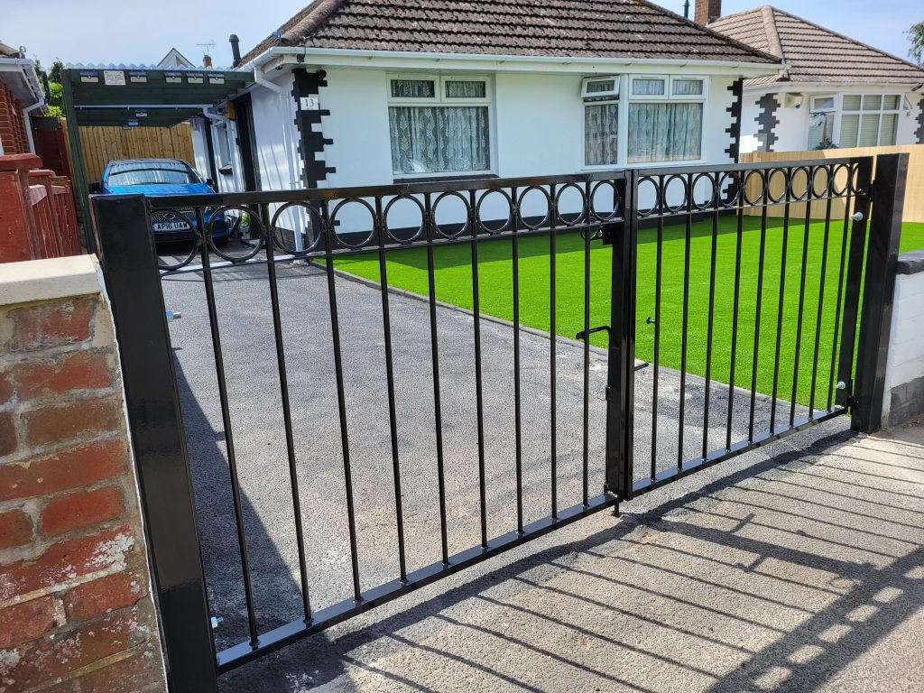 Black metal double gates with a row of rings along the top rail across a bungalow driveway